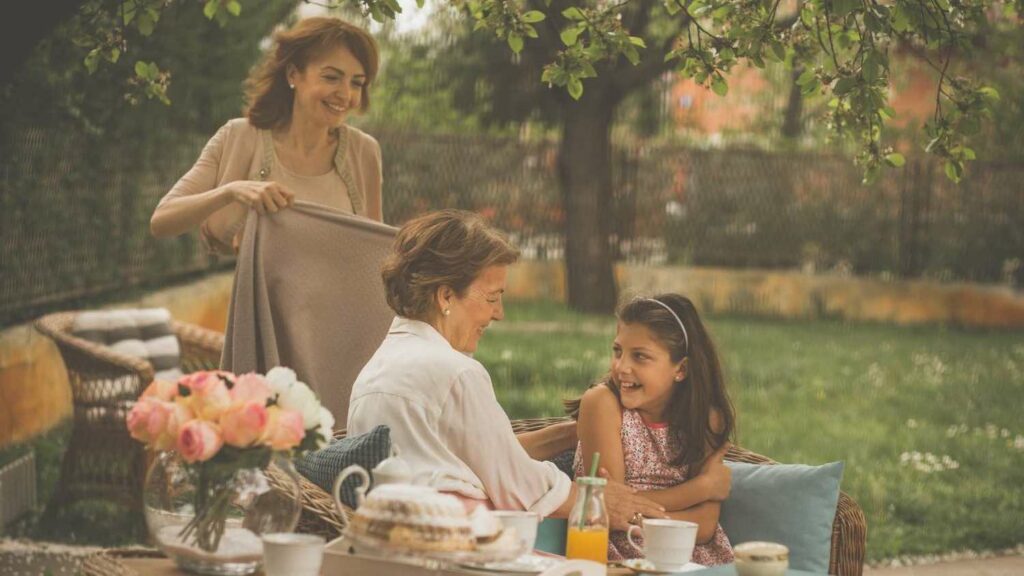 two women and a young girl sitting outside in the yard with juice and coffee